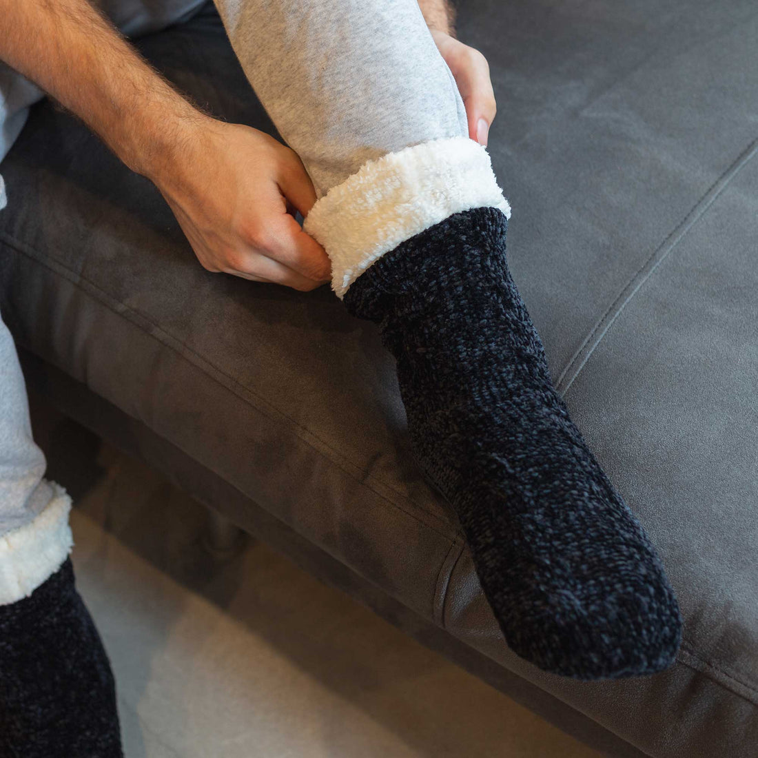 The Foozie™ in Black, a man on the sofa folding the fluffy sherpa cuff down over his leg
